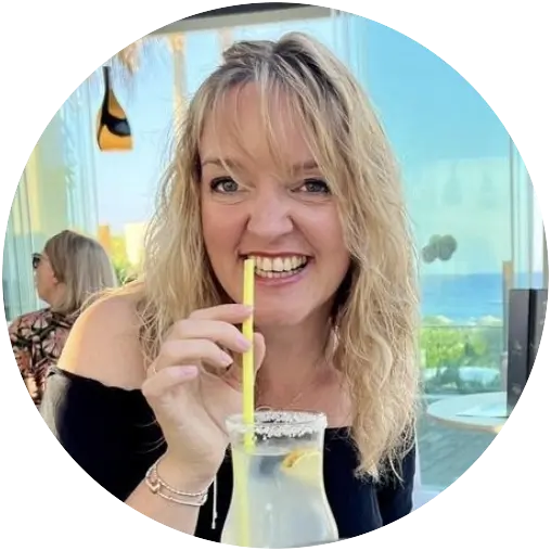 The image features Emma Hartley, a travel consultant at Harmony Voyages, enjoying a cocktail while on holiday. She is seated at an outdoor table, surrounded by a scenic resort backdrop. Emma has a cheerful smile, and her relaxed demeanor conveys a sense of enjoyment and leisure. This image captures Emma's passion for travel and the enjoyment of experiencing new destinations.