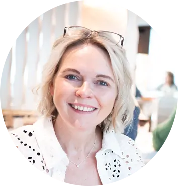 The image features Angela Schofield, a director at Harmony Voyages, smiling warmly at the camera. She has shoulder-length hair and is dressed in a professional outfit, exuding a friendly and approachable demeanor. The background is softly blurred, keeping the focus on her. This portrait captures her confidence and leadership within the Harmony Voyages team.